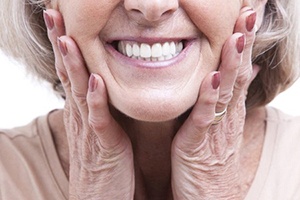 smiling woman with dental implants holding her cheeks